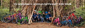   A group of kids take shelter in the forest inside their newly-built den with their bikes propped up outside. 